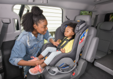 An adult adjusting the seatbelt of a young child in a front-facing car seat.