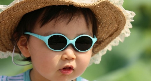 young child sitting in the sun with a straw hat and glasses