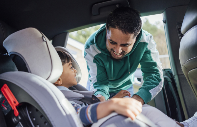 An image of a man buckling a young boy into a car seat.