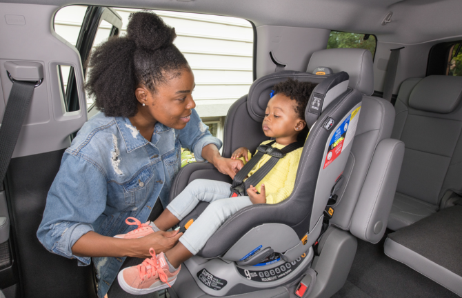 An adult adjusting the seatbelt of a young child in a front-facing car seat.