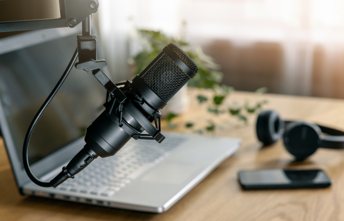 A microphone, a laptop, a headset, and a cell phone on a wooden table.