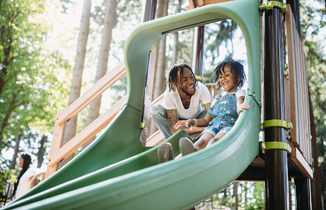 Father helping daughter down a playground slide