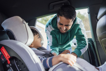 An image of a man buckling a young boy into a car seat.