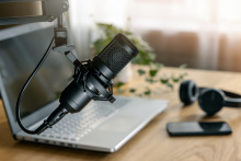 A microphone, a laptop, a headset, and a cell phone on a wooden table.